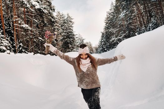 A girl in a sweater in winter with a bouquet in her hands stands among large snowdrifts.