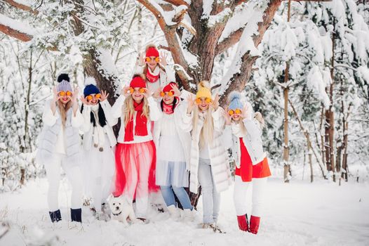 A large group of girls with tangerines are standing in the winter forest.Girls in red and white clothes with fruit in a snow-covered forest.