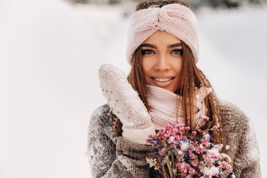 A girl in a sweater in winter with a bouquet in her hands stands among large snowdrifts.