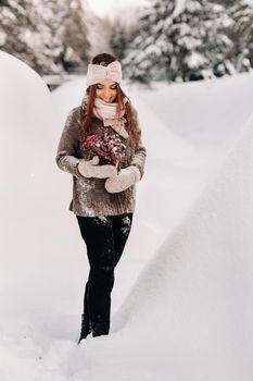 A girl in a sweater in winter with a bouquet in her hands stands among large snowdrifts.