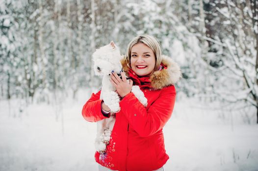 Portrait of a woman in a red jacket with a dog in a cold winter forest. A girl holds a dog in her hands in a snow-covered winter forest