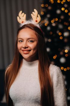 Girl for Christmas with reindeer horns in the home interior.A woman on New year's eve in a white sweater and skirt.