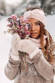 A girl in a sweater in winter with a bouquet in her hands stands among large snowdrifts.