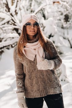 A girl in a sweater and glasses in winter in a snow-covered forest.