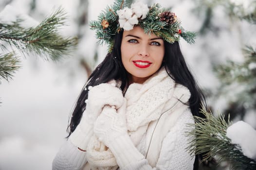 Portrait of a woman in white clothes in a cold winter forest. Girl with a wreath on her head in a snow-covered winter forest.