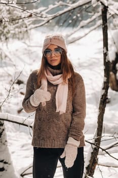 A girl in a sweater and glasses in winter in a snow-covered forest.