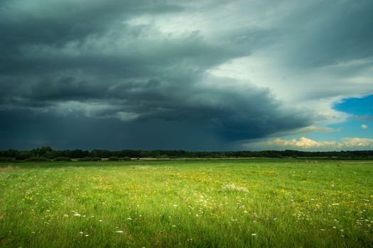 View of the dark thundercloud above the green meadow