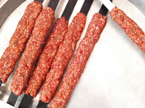 Raw Lula kebab on skewers lies on white plate, ready for grilling, close-up