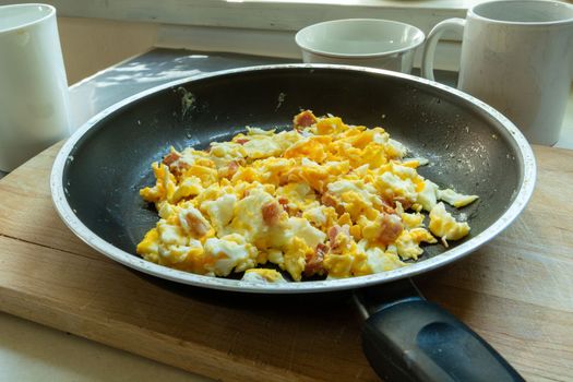 Morning scrambled eggs with bacon in a pan, close up