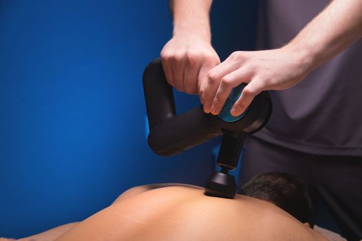 Close-up of a percussion massage of the neck muscles to an athlete in a medical office in the gym. Percussion therapy for the regeneration of the sports body and rehabilitation after injuries. copy space.