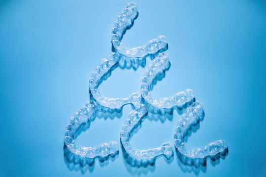Close up, invisible aligners on a blue background in the shape of a pyramid or triangle creating a pattern. Plastic braces for teeth alignment.