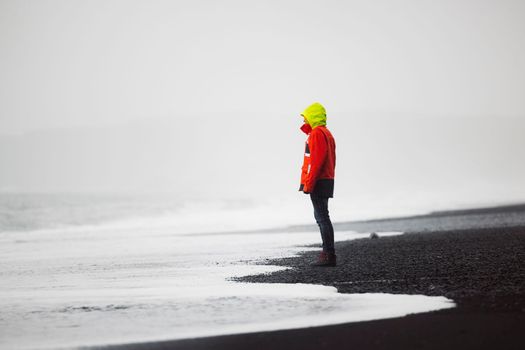 The man in waterproof jacket and pants standing on the beach with black volcanic sand, Reynisfjara, south of Iceland. Icelandic nature, Atlantic Ocean shore, seaside. High quality photo