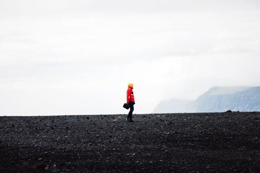 A traveler in a red jacket standing on a black sand beach in Iceland. One person only, cold foggy Icelandic weather.