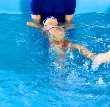 Male Trainer teaching preschool girl how to swim on the back in indoor pool