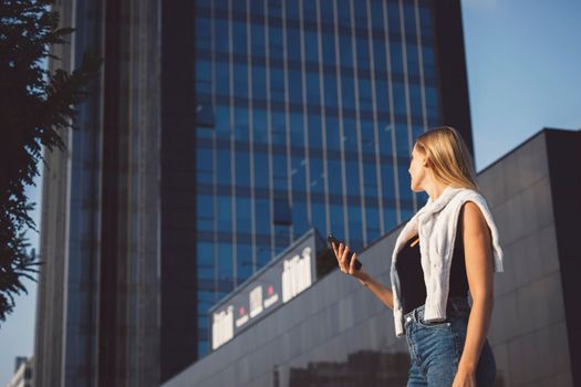 Young caucasian woman in an urban modern setting, skyscrapers in the bacground, using a mobile device. Business woman on a break.