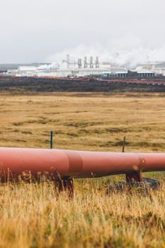 Geothermal Power Plant, hot water power station in Iceland. Steam rolling out of the plant chimneys, red large tubes running across the grounds filled with hot water. Sustainable, energy efficient Cloudy cold autumn day in Iceland.