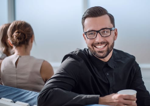 young businessman with a Cup of coffee sitting in a modern office. coffee break