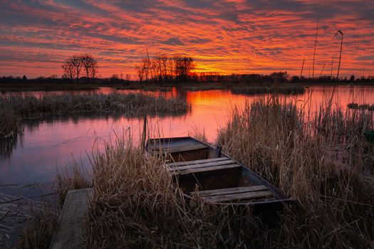 An old boat in the reeds on the lake shore and a beautiful sunset, Stankow, Poland