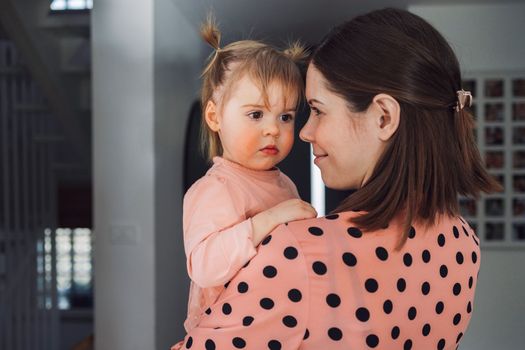 Young caucasian woman, mom, spending time with her toddler, young girl wearing a pink dress matching her mom. Mom and daughter decorating for Christmas together having fun. Mom holding a smiling little girl in her arms.