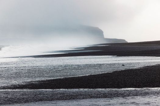 Volcanic Black Sand Beach with a view of Reynisdrangar. Waves crashing on the black sand beach. Vik, Iceland. High quality photo