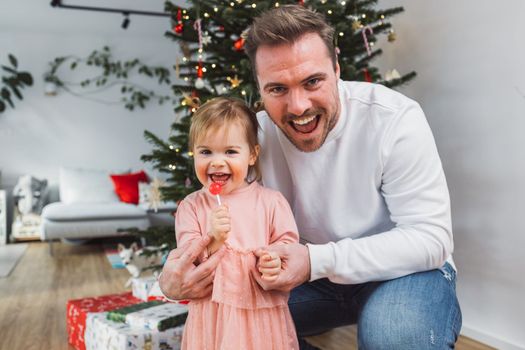 Portrait of young caucasian man with his daughter, decorating the Christmas tree. Loving dad having fun with his little girl on Christmas.