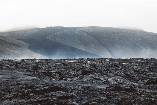 Geldingadalir active Volcano, errupting in 2021 - Fagradalsfjall and 2022 -Meradalir. Still hot lava rocks, steam comping up from the grounds. Dark grey, black volcanic rocks in Iceland. Dramatic view of lava rocks cold cloudy autumn day in Iceland.