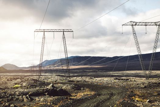High voltage electrical cables on poles, with a backdrop of a cloudy sky. The lines are attached to the poles with glass insulation. The lines are running through the Icelandic highlands. High quality photo