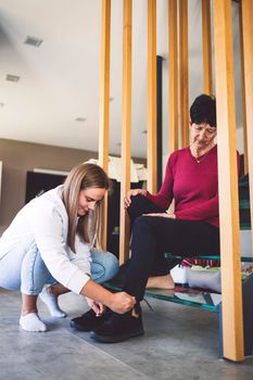 Young caucasian woman a nurse, on a home visit taking care of a senior lady. Nurse helping a senior women with every day chores, helping her to walk and move around the house.