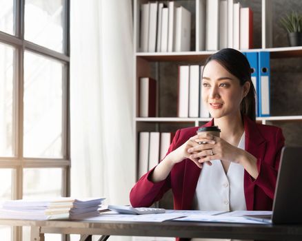 Young Asian american business woman sitting with laptop and cup of coffee.