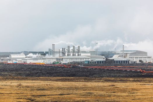 Geothermal Power Plant, hot water power station in Iceland. Steam rolling out of the plant chimneys, red large tubes running across the grounds filled with hot water. Sustainable, energy efficient Cloudy cold autumn day in Iceland.