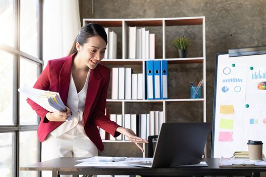 Cheerful young woman working with laptop and documents.