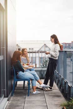Young caucasian woman college students, sitting on the rood top of their dorm room, eating a snack taking a break from studying, getting some fresh air, on a cloudy autumn day.