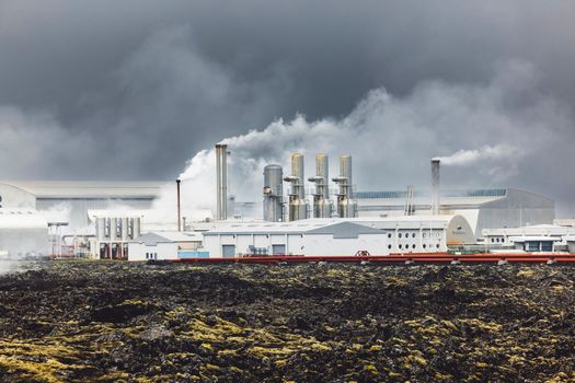 Geothermal Power Plant, hot water power station in Iceland. Steam rolling out of the plant chimneys, red large tubes running across the grounds filled with hot water. Sustainable, energy efficient Cloudy cold autumn day in Iceland.