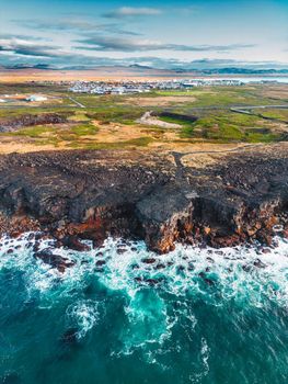 Small fishing town in the distance and waves crushing to the shore. Vertical photo, autumn 2022.