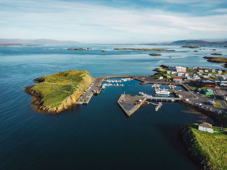 Beautiful aerial view of the Stykkisholmskirkja Harbor with Fishing ships boats at Stykkisholmur town in western Iceland. City view from Sugandisey Cliff with lighthouse. Famous colorful houses. September, autumn 2022.