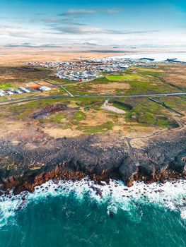 Small fishing town in the distance and waves crushing to the shore. Vertical photo, autumn 2022.