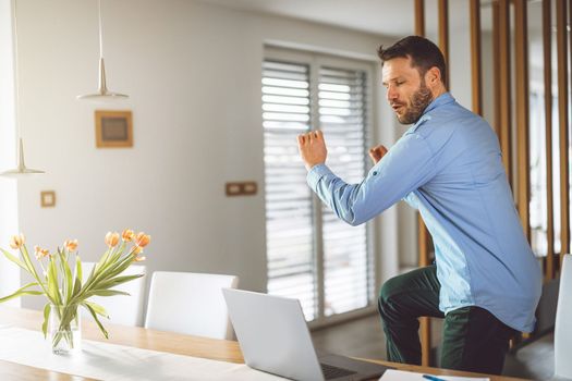 Excited caucasian man cheering for his team, watching a football game on his laptop, man celebrating a win with clenched fists.