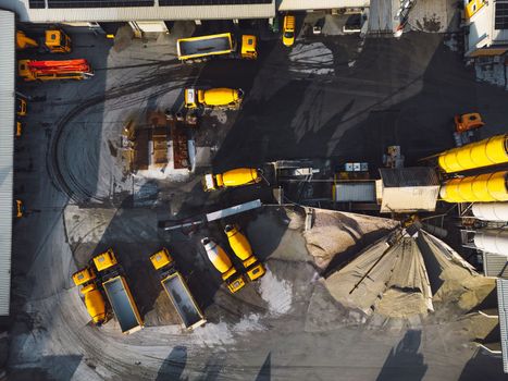 Aerial view in industrial area, directly above concrete plant, firm with lots of heavy machinery on the grounds, yellow trucks and other vehicles.