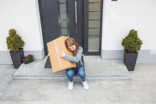 Thrilled caucasian woman sitting down at the front door with a big cardboard box that just came in the mail. Woman receiving an exciting package.