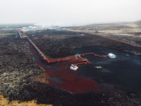 Geothermal Power Plant, hot water power station in Iceland. Steam rolling out of the plant chimneys, red large tubes running across the grounds filled with hot water. Sustainable, energy efficient Cloudy cold autumn day in Iceland.