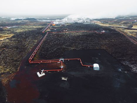 Geothermal Power Plant, hot water power station in Iceland. Steam rolling out of the plant chimneys, red large tubes running across the grounds filled with hot water. Sustainable, energy efficient Cloudy cold autumn day in Iceland.