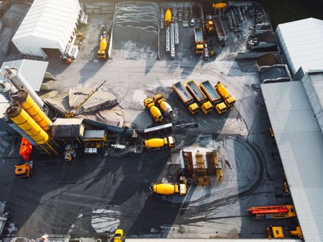 Aerial view in industrial area, directly above concrete plant, firm with lots of heavy machinery on the grounds, yellow trucks and other vehicles.