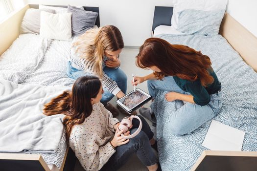 Group of three roommates, college student, young caucasian women, spending time together in their room, studying, talking, having fun, laughing.