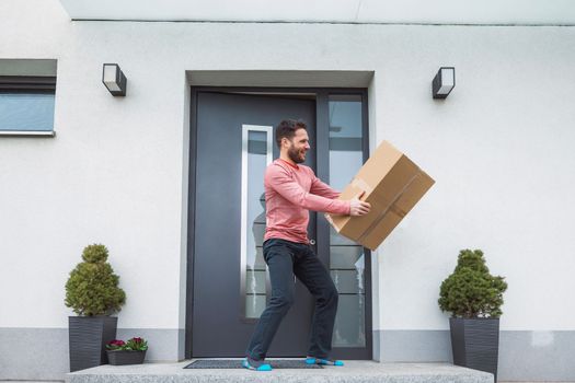Thrilled caucasian man standing at the front door with a big cardboard box in his hands that just came in the mail. Man receiving an exciting package.