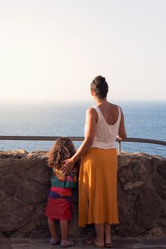 mother and daughter looking at the horizon facing the sea. vertical photo, copy space