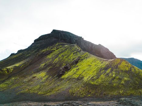 Remote volcanic lands somewhere in Iceland mainland, surrounded by vibrant green bushes and volcanic lands. Volcanic rock formations, small mountains, black grey volcanic rock. No people.