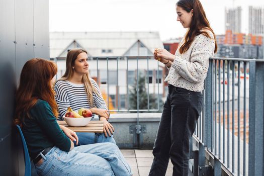 Young caucasian woman college students, sitting on the rood top of their dorm room, eating a snack taking a break from studying, getting some fresh air, on a cloudy autumn day.