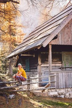 Young caucasian woman hiker sitting on a wooden fence somewhere in the autumn forest while on a hike, wearing a bright yellow shirt and colorful leggings.