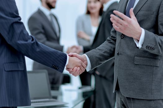 Business partners handshaking over their colleagues on background.