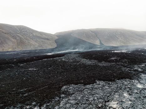 Geldingadalir active Volcano, errupting in 2021 - Fagradalsfjall and 2022 -Meradalir. Still hot lava rocks, steam comping up from the grounds. Dark grey, black volcanic rocks in Iceland. Dramatic view of lava rocks cold cloudy autumn day in Iceland.